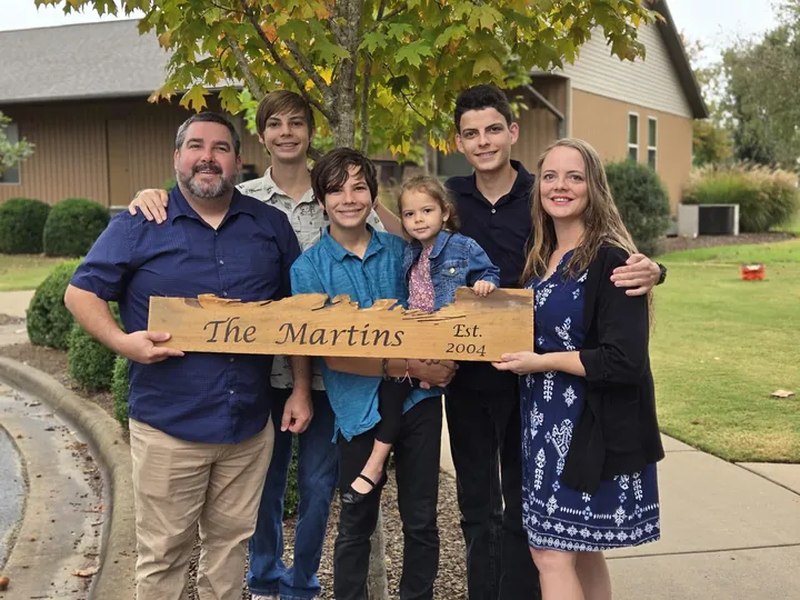Max and Tara with their family, holding a wooden sign that reads “The Martins, Est. 2004”