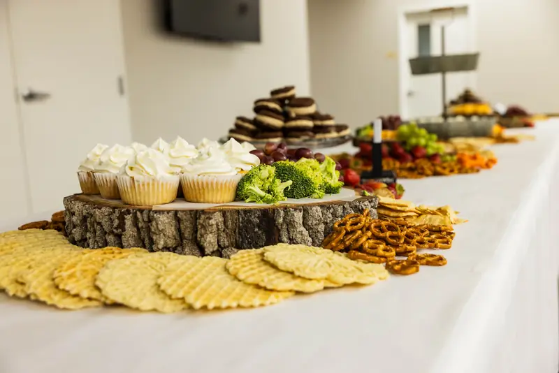 A long table of light snacks: cupcakes, fruit, pretzels, and cookies