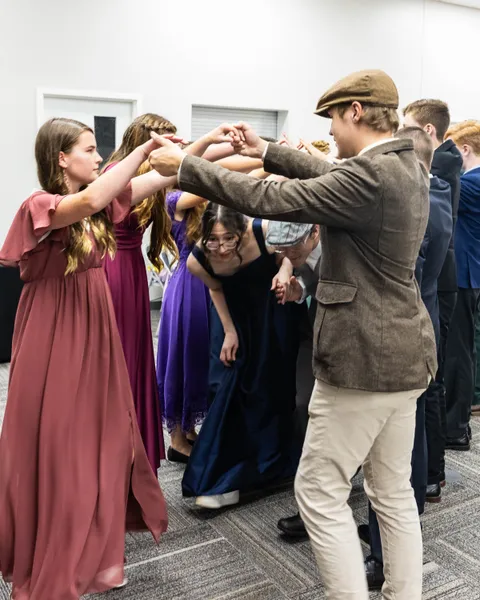 Dancers in gowns and jackets ducking through an arch of raised hands