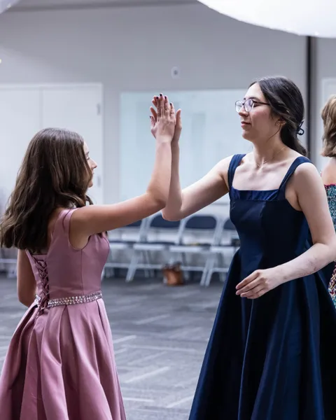 Two ladies in gowns meeting palm to palm during a dance