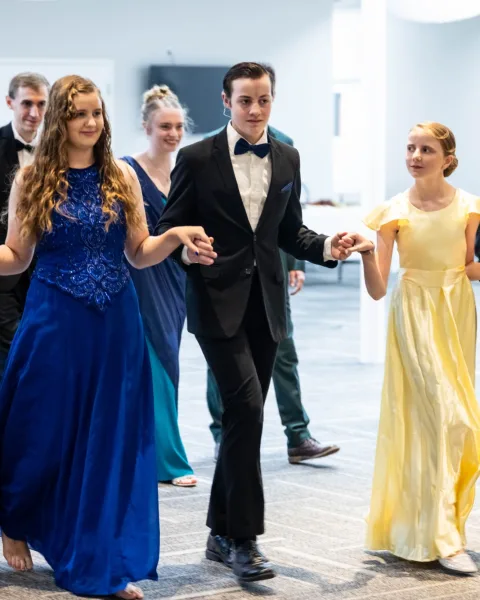 Ladies in gowns and gentlemen in suits walking hand in hand during a dance